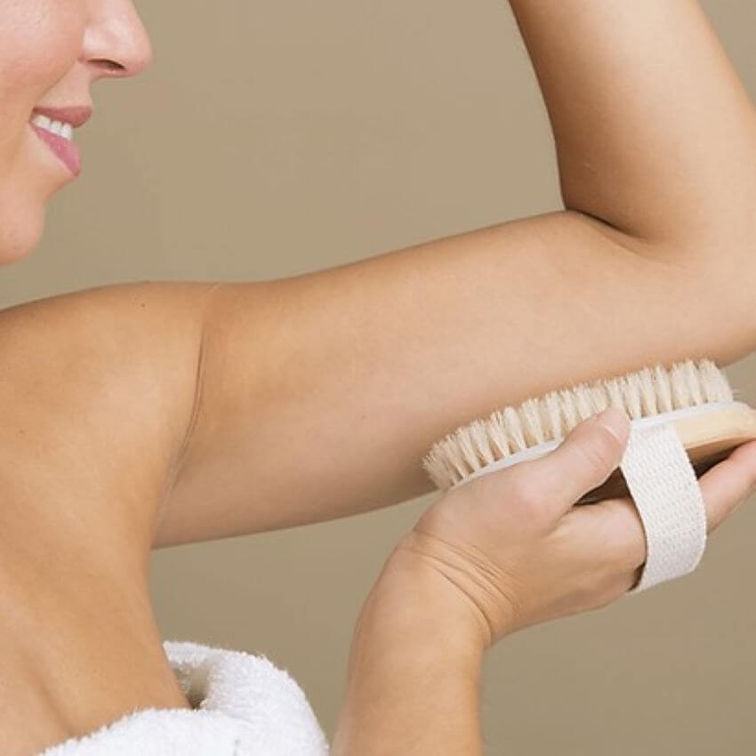 Woman wrapped in towel using dry brush on arm for blog: GLOWING SKIN SECRET: DRY BRUSH TECHNIQUE REVEALED