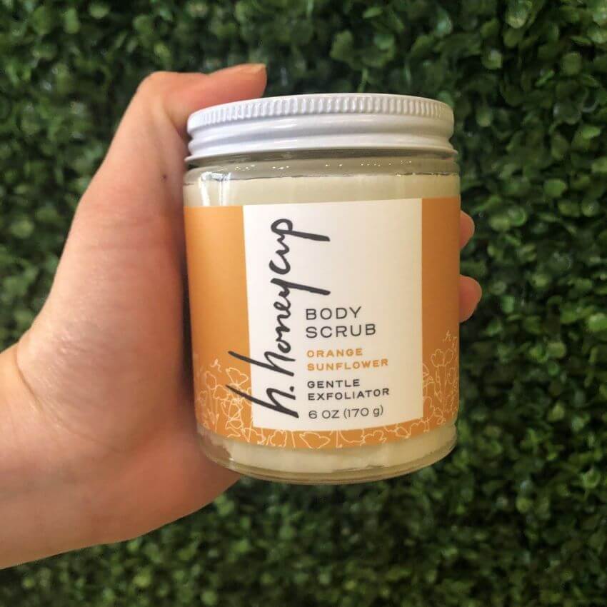 Woman holding orange body scrub up to natural green background for blog: WINTER SKINCARE: 5 STEPS TO AVOID DRY SKIN