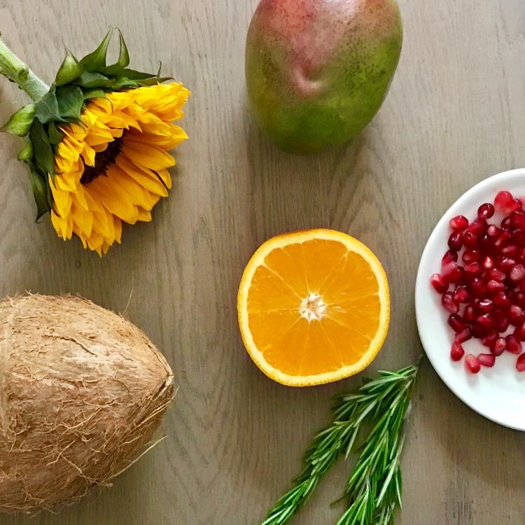 Image of actual fruit, flower and herbs in H. Honeycup skincare. Natural skincare ingredients are food grade. Sunflower, mango, orange, rosemary, pomegranate and coconut. For blog describing how essential oils and carrier oils are used in skincare.
