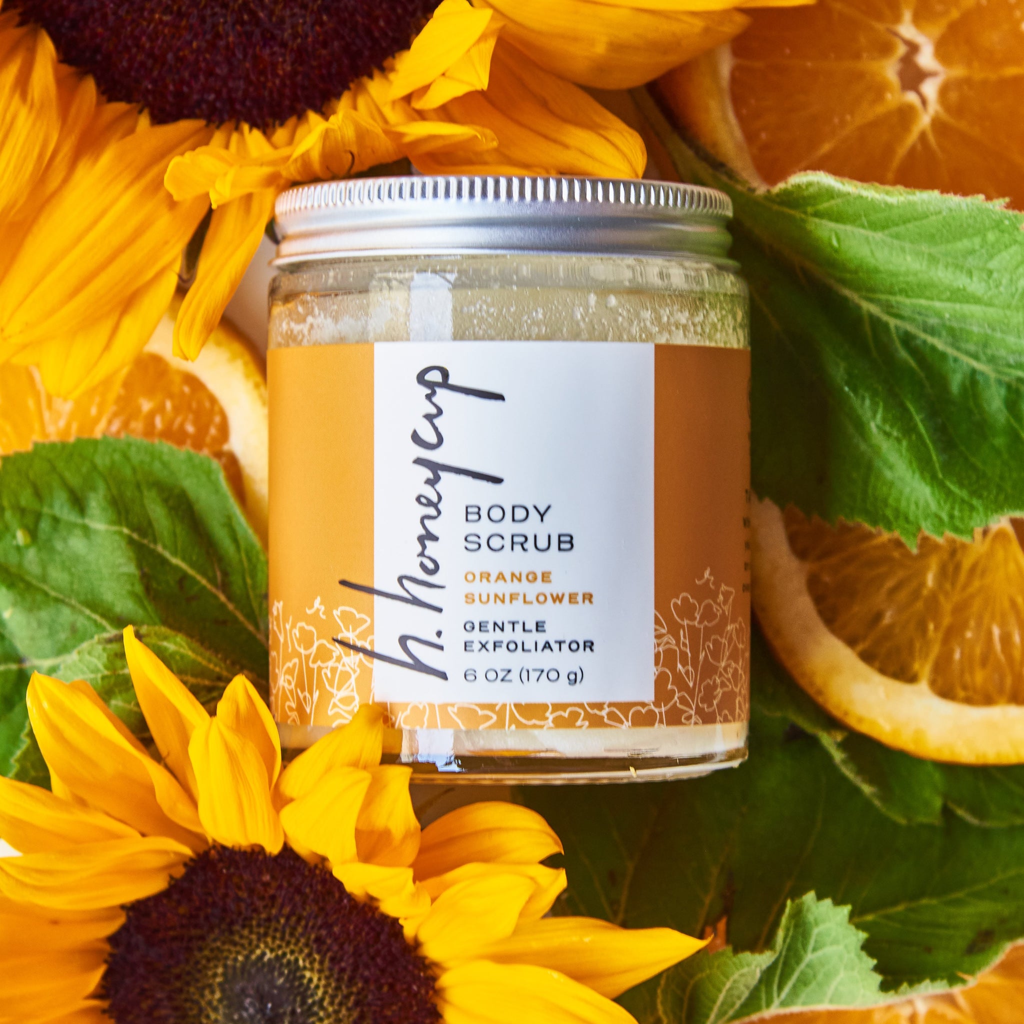 Body scrub surrounded by real oranges and sunflower ingredients