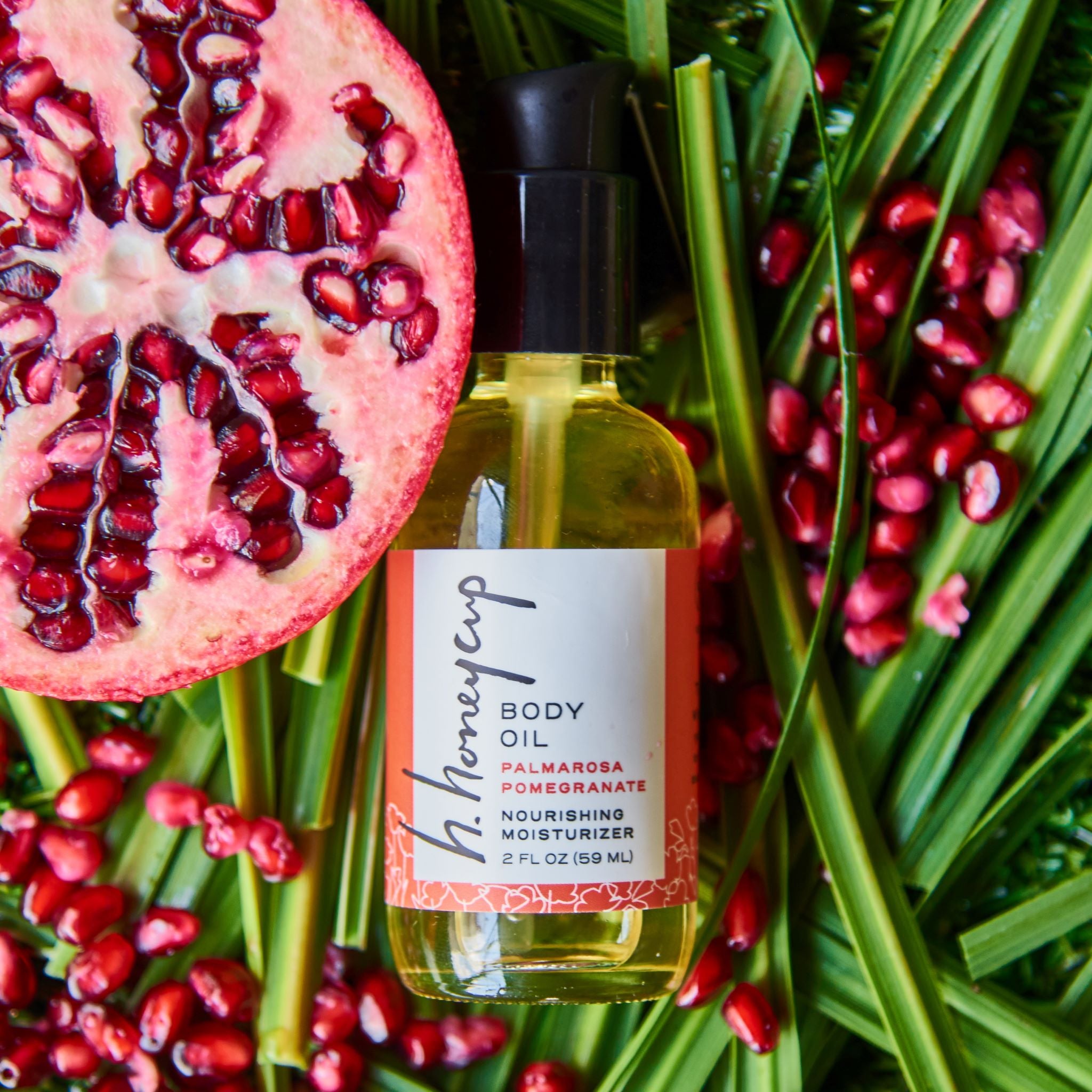Body oil surrounded by real pomegranates and palmarosa ingredients