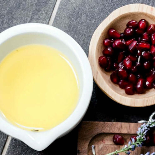 Image of H. Honeycup lavender and palmarosa natural body oil in small bowl and pomegranate seeds in small wooden bowl for blog on essential oils vs "fragrance" as scent in natural skincare