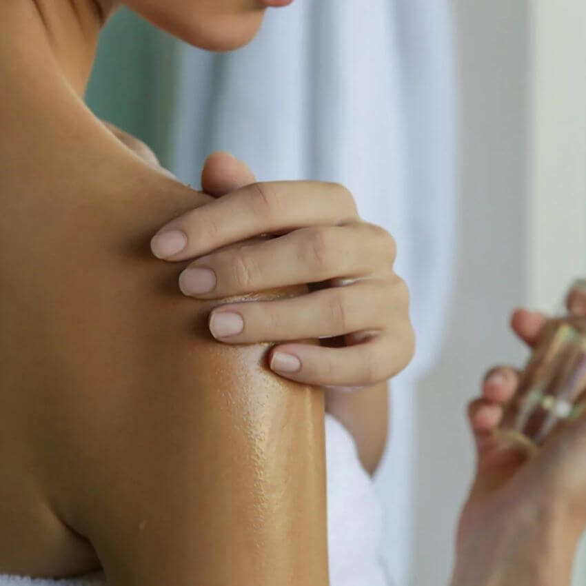Woman rubbing lotion on shoulder - MASTERING BODY OIL VS. BODY LOTION YEAR-ROUND