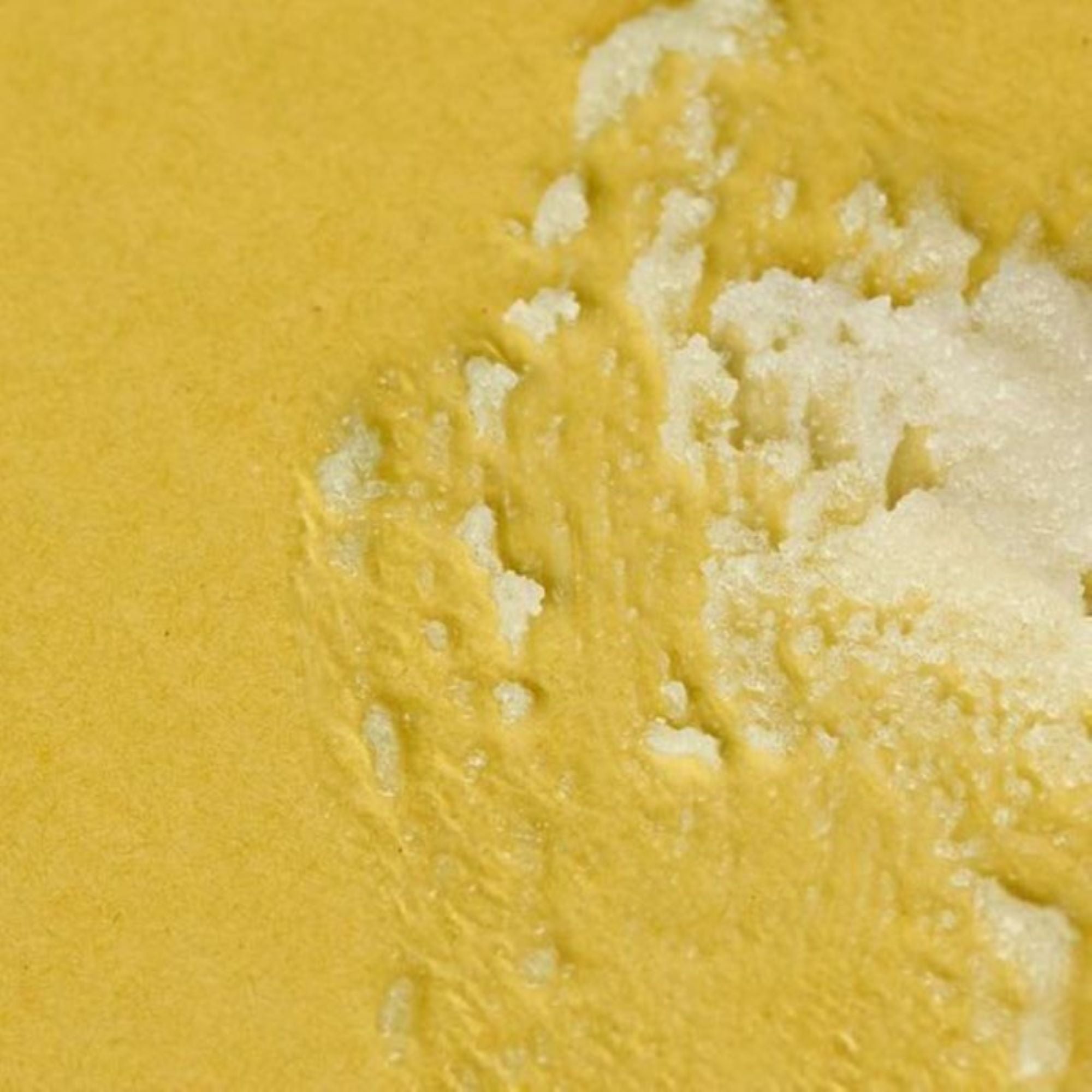 H. Honeycup body scrub smeared on yellow background to show sugar texture